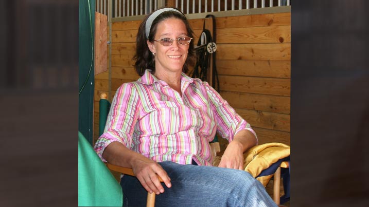 photo of Ann Hill sitting in a horse stall.