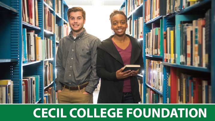 Two students standing between shelves of books.