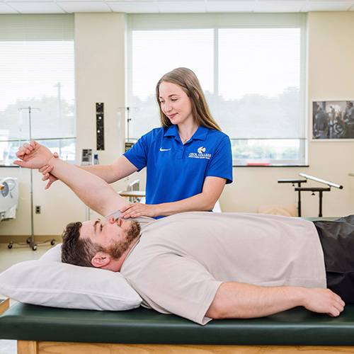 Female Cecil College Physical Therapist Assistant student practicing therapy on male student who is prone on therapy table