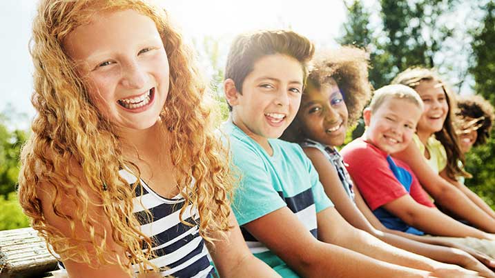 There is a group of young children sitting on a bench smiling and looking at the camera.