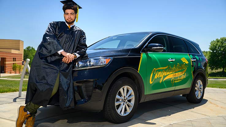 A graduate student leans against a car.