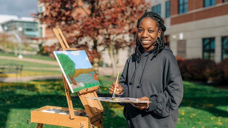 An art student at an easel with paint and a brush.