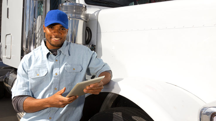 A truck driver leaning on a semi truck.