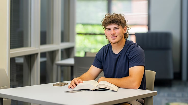 A student reading a book at a table.