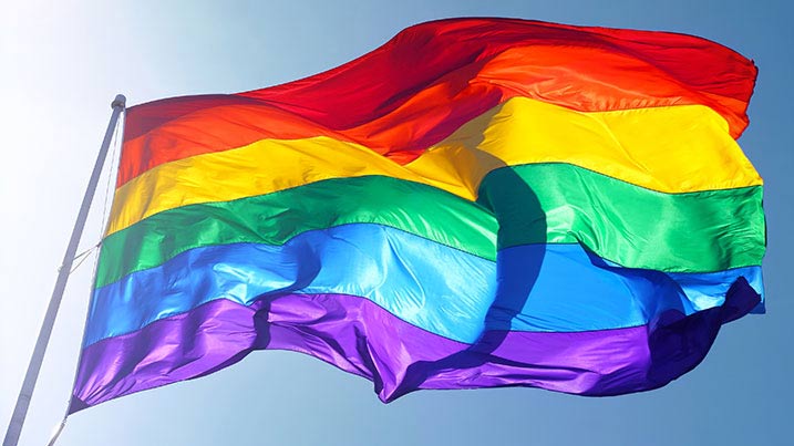 Pride flag set against a blue sky.